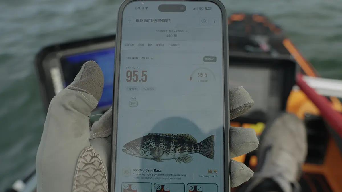 An angler on a kayak checking a QuickCast scorecard in the HOOKED app